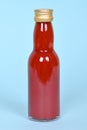 Hot red chilly sauce in little glass bottle on blue background. Royalty Free Stock Photo