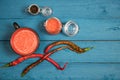 Hot red pepper sauce in a glass jar and Cup on a wooden blue background, pepper pods lying next to each other. Royalty Free Stock Photo