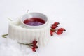 Hot red tea in the snow, cup with scarf and rose hips, white snowy background with copy space, hot drink against flu Royalty Free Stock Photo