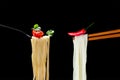 Hot spagetti on the fork with tomato and parsley and Asian noodles on chopsticks with red pepper. Royalty Free Stock Photo