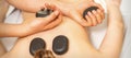 Hot stone massage on the female back with hands of masseur holding black massage stones in spa salon. Royalty Free Stock Photo