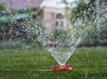 Hot summer day. The fountain waters the green grass on the lawn