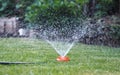 Hot summer day. The fountain waters the green grass on the lawn