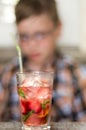 Hot summer vacation concept. Refreshing mint cocktail on a cafe table with a blurred teenage boy reading in the background.