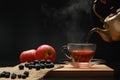 The hot tea fruits in glass cup with pouring from the golden teapots with smoke and blueberry, apple on the wooden board. Royalty Free Stock Photo