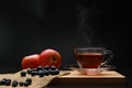 The hot tea fruits in glass cup with smoke and blueberry, apple on the wooden board as black background. Healthy drink concept. Royalty Free Stock Photo