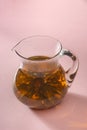 Hot tea in a glass jug on pink background. Thousand year red tea flowers
