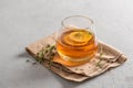 Hot tea in a glass with lemon and thyme on a linen napkin, gray background with copy space. Autumn and winter traditional drinks