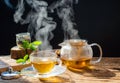 Hot tea in glass teapot and cup with steam on wooden table, black background Royalty Free Stock Photo