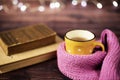 Hot tea, hot chocolate, coffee in yellow cup, wrapped with a pink knitted scarf. Old books. Blurred lights, wooden background Royalty Free Stock Photo