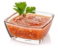 Hot tomato sauce with parsley leaves in a small transparent glass square bowl isolated on white background