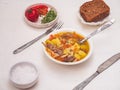 Hot turkey soup with spices and pasta in a deep plate on a white table, cutlery laid out next.