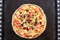 Hot vegetarian pizza with tomatoes, bell pepper, onion, black olives, cheese, spices on dark black baking tray background close up