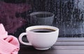 A hot white coffee cup and pink sweater on a vintage wooden window sill or a window table with raindrops on a glass background Royalty Free Stock Photo