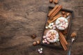 Hot winter or autumn drink with cocoa, chocolate, spices and marshmallows in cups on vintage wooden background with knitted warm