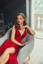 Hot young adult and imperious woman, dressed in a long scarlet red long dress, sexually shows her nude elegant leg Royalty Free Stock Photo