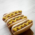 Hotdog with yellow mustard on rustic wooden board on white wooden table, low angle view. Space for text Royalty Free Stock Photo