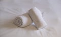 Hotel bedroom. White fluffy, rolled towels and linen sheets on a bed. Close up view Royalty Free Stock Photo