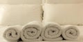 Hotel bedroom. White fluffy, rolled towels in row, linen sheets and pillows on a bed. Closeup. Royalty Free Stock Photo