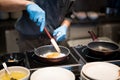 Hotel chef hands with gloves cooking fried eggs on hot pan for b