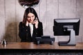 Hotel receptionist. Modern hotel reception desk with bell. Happy female receptionist worker standing at hotel counter and talking Royalty Free Stock Photo