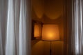 Hotel room with orange lit abat-jour, framed mirror and white curtains