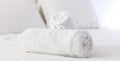 Hotel`s bedroom. White fluffy, rolled towels, linen sheets and pillows on a bed. Close up view. Royalty Free Stock Photo