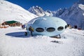 Hotel in the shape of an alien flying saucer standing high in the mountains among the snow capped mountain peaks. Dombay