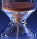 Hour Glass with running sand inside, on blue background. Time passing or countdown concept Royalty Free Stock Photo