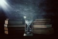 Hourglass as time passing concept and old books in front of black wall background. Conceptual photo on history, fantasy and