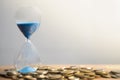 Hourglass blue sand and stack of coins.