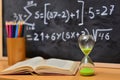 Hourglass and book on a table, with a blackboard background