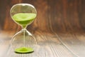 Hourglass with falling sand inside a glass bulb on a wooden daylight background