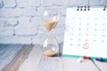 hourglass flowing through the bulb of sandglass and calendar on table