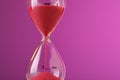 Hourglass with flowing red sand on violet background, closeup. Space for text Royalty Free Stock Photo