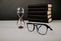 Hourglass with glasses and books on a grey table