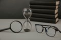 Hourglass with glasses, magnifier and books on a desk