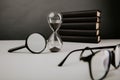 Hourglass with glasses, magnifier and books on a table