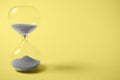Hourglass with gray sand on yellow background