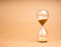 Hourglass on light brown recycled paper background with copy space. Golden sand in sandglass clock isolated on eco kraft paper Royalty Free Stock Photo