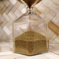 Hourglass made of clear glass, with gold beads. Sand pours down from top to bottom. Object on a wooden background of natural color