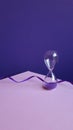 Hourglass made of transparent glass, purple serpentine on purple background.