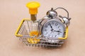 An hourglass and a metal alarm clock in the shopping basket. concept of time