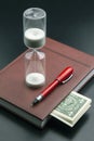 Hourglass, money, pen and notebook are on the table. Business office items. Time is money. Business solutions in time