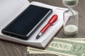 Hourglass, money, pen and notebook are on the table. Business office items. Time is money. Business solutions in time