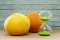 Hourglass with orange and grapefruit on a wood background, close-up