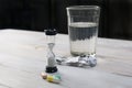 Hourglass, pills and glass of water on wood table. limited lifetime