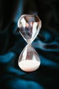 An hourglass with pink sand at the bottom of the clock is on a blue satin background. The concept of stopped time. Royalty Free Stock Photo