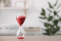 Hourglass with red flowing sand on table against blurred background. Space for text Royalty Free Stock Photo