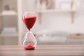 Hourglass with red flowing sand on table against blurred background. Space for text Royalty Free Stock Photo